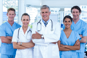 Team of doctors standing arms crossed and smiling at camera in medical office